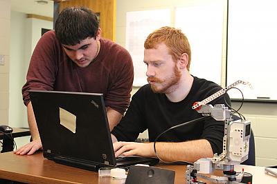 Two students work on controlling LEGO robotic arm via laptop