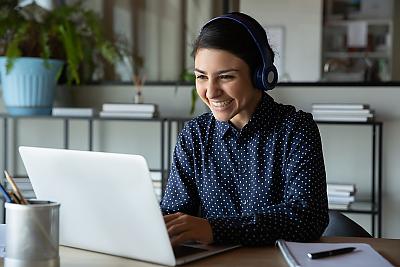 Female student in blue sitting at table in front of laptop and smiling at computer