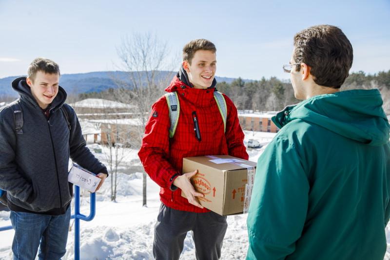 Photograph of winter scene of two 具有里程碑意义的大学 students holding mailed packages while third student looks on.